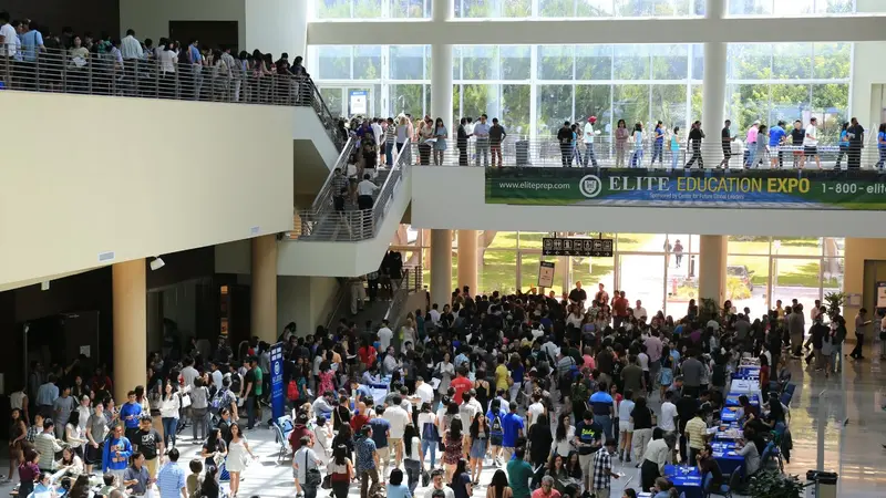 Crowds fill a convention center atrium beneath a banner reading "Elite Education Expo" during a college fair.