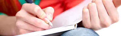 Close-up of a student's hands writing in a notebook with a pen