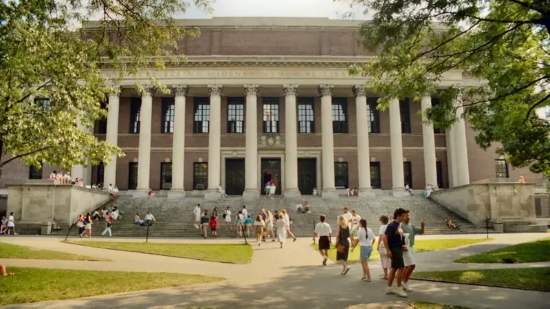Students walking and sitting on the steps of a large columned university library building on a sunny day.