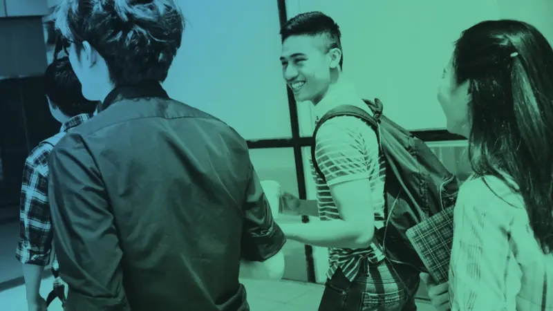 Students chatting in a hallway, one smiling and wearing a backpack, in a green-tinted photo.
