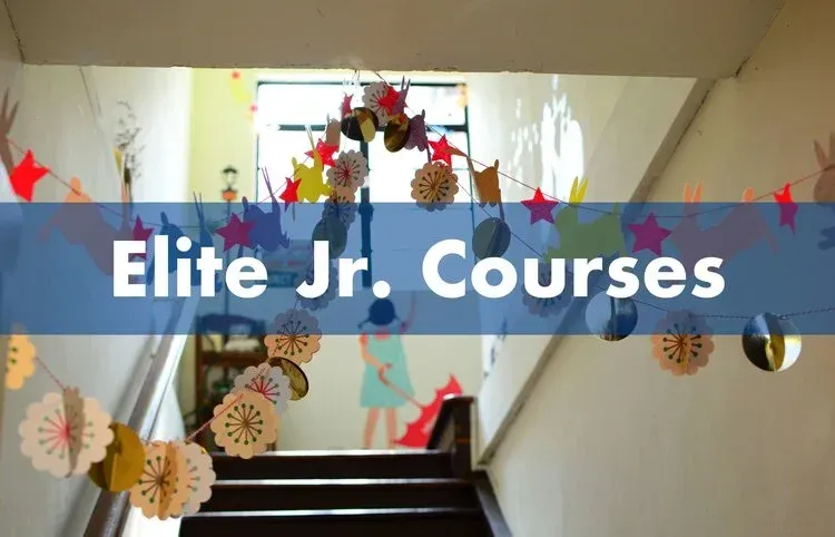 Paper garlands of stars and flowers strung above a stairwell, with the banner text "Elite Jr. Courses".