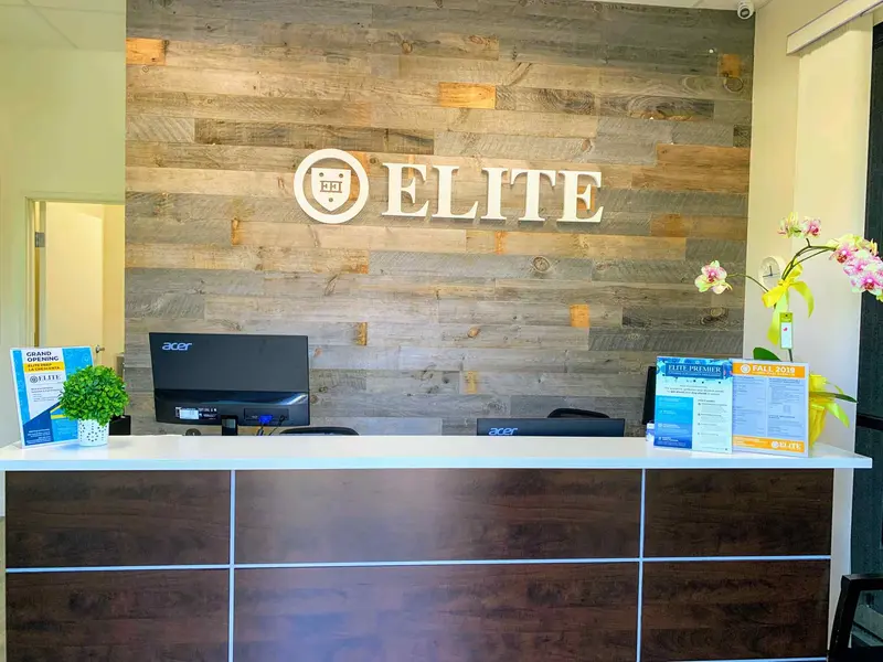 Reception desk with computers, brochures and orchids in front of a reclaimed wood wall bearing the ELITE logo.