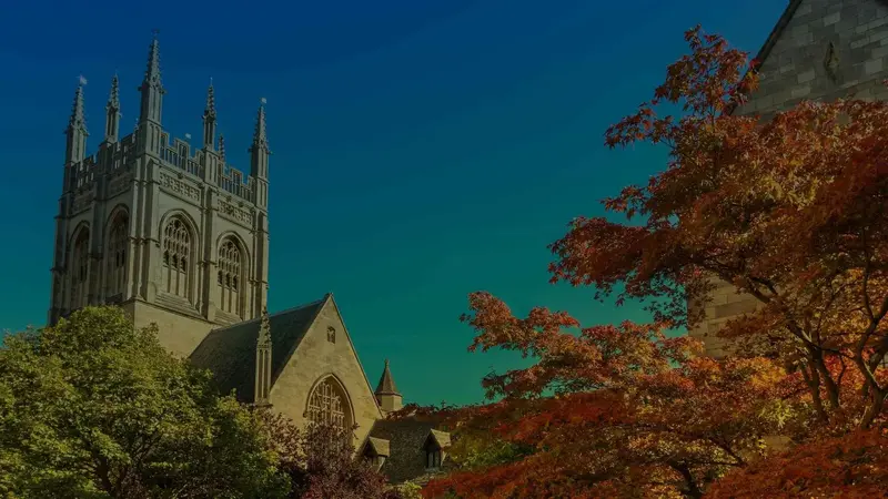 Gothic stone chapel tower against a deep blue sky, framed by green and autumn-red trees