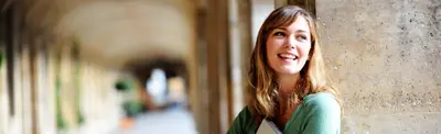A smiling young woman leaning against a stone column in a sunlit archway walkway