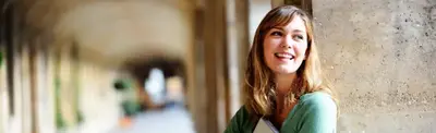 A smiling young woman leaning against a stone column in a sunlit archway walkway