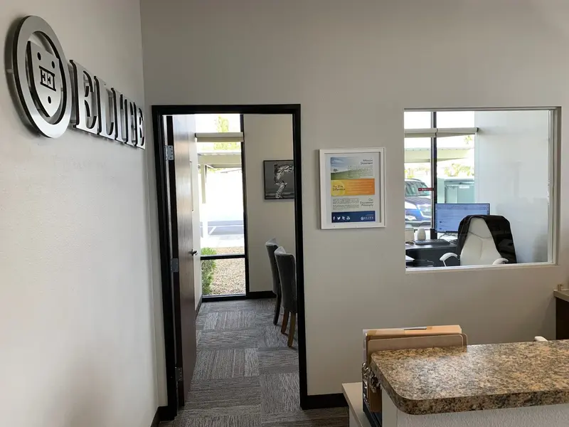 Office interior with an "Elite" logo on the wall, an open doorway, and an interior window overlooking a desk and chair