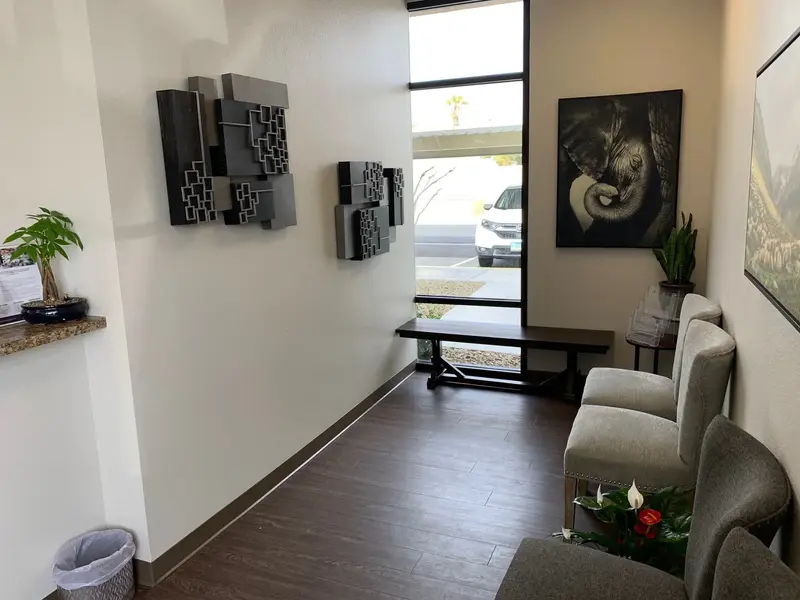 Office waiting area with gray armchairs, elephant artwork, wall sculptures, bench, and a window onto a parking lot.