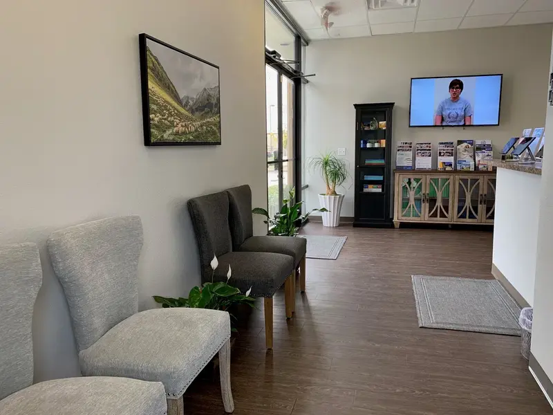 Waiting area with upholstered chairs, a framed mountain landscape, brochure display cabinet, and a wall-mounted TV.