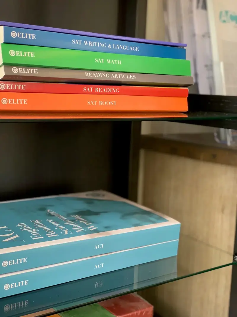 Stacked Elite prep books on glass shelves, labeled SAT Writing & Language, SAT Math, Reading Articles, SAT Reading, SAT Boost, and ACT.