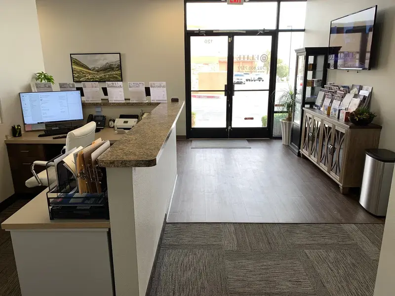 Office lobby with a granite reception counter, computer workstation, brochure display cabinet, and glass entrance doors.