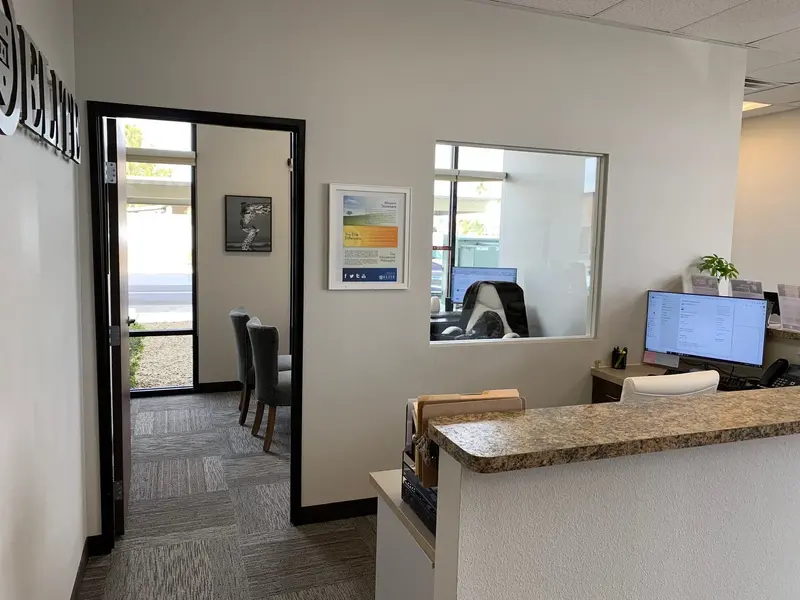 Office interior with reception desk, computer monitor, interior window into a classroom, and a doorway to a waiting area