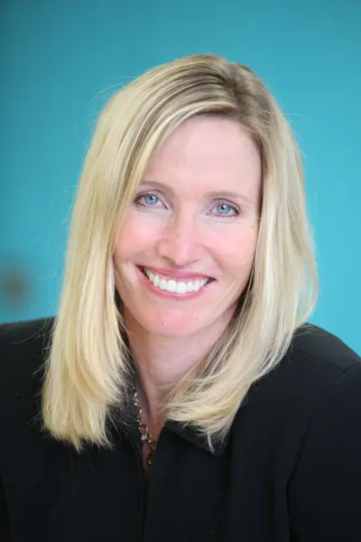 Smiling blonde woman in a black jacket against a turquoise background