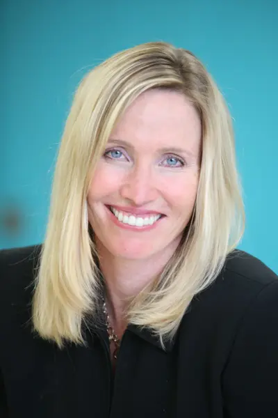 Smiling blonde woman in a black jacket against a turquoise background