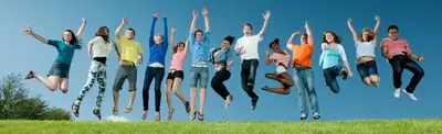 A group of teenagers jumping in the air with arms raised on a grassy hill under a blue sky