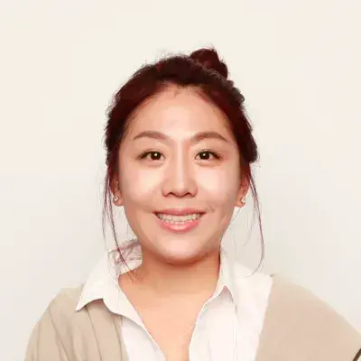 Smiling woman with her hair in a bun, wearing a white collared shirt and tan cardigan
