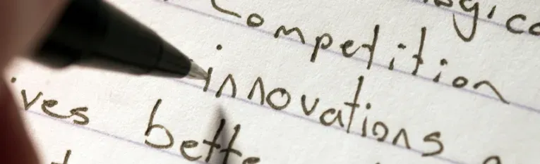 A pen resting on lined paper with handwritten words including "competition," "innovations" and "better".