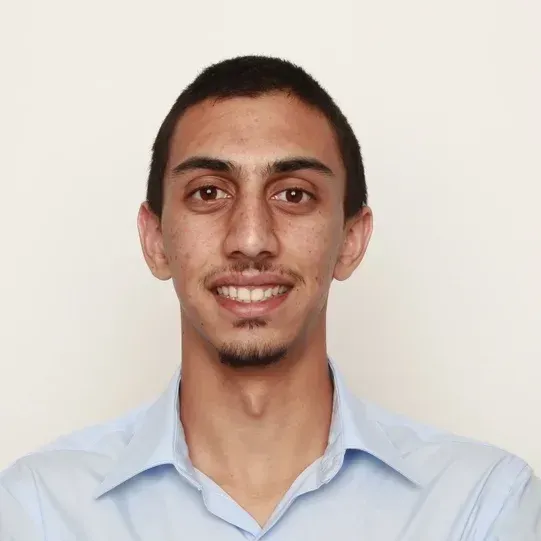 Smiling young man with short dark hair and a light blue collared shirt against a plain background