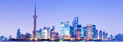 Shanghai skyline at dusk, with illuminated skyscrapers and a tall spired tower reflected in the river