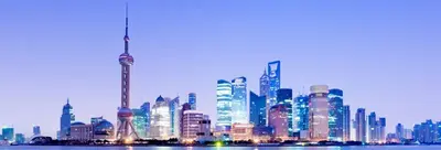 Shanghai skyline at dusk, with illuminated skyscrapers and a tall spired tower reflected in the river
