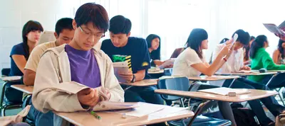 Students at desks in a classroom working through workbooks and study materials
