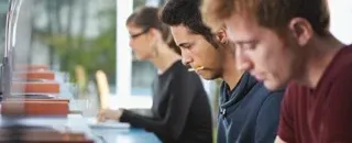 A row of students working side by side at computers in a classroom.