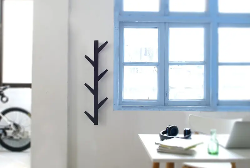 Bright room with a blue-framed window, black branch-shaped wall hook, and a white desk holding headphones, papers and a laptop