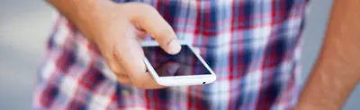 A person in a red and blue plaid shirt holding a white smartphone in both hands