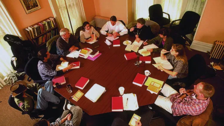 About ten students and a professor seated around a large wooden table with books and papers in a small seminar room