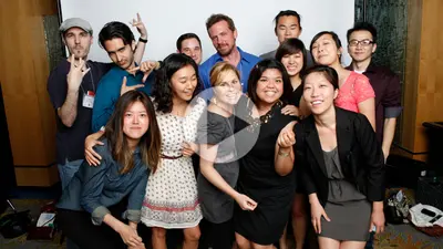 A group of smiling young students posing together, with a video play button overlaid on the photo.