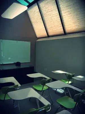 녹색과 흰색 책상, 화이트보드, 경사진 천장의 채광창이 있는 빈 교실