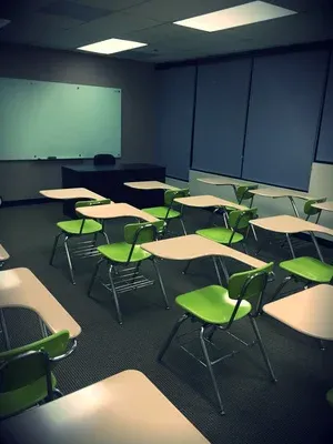 초록색 책상 의자가 줄지어 놓인 빈 교실과 화이트보드, 프로젝터 스크린이 보이는 모습