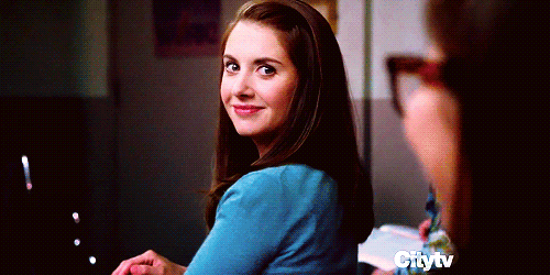 A woman in a blue top turns to look over her shoulder with a knowing smile.