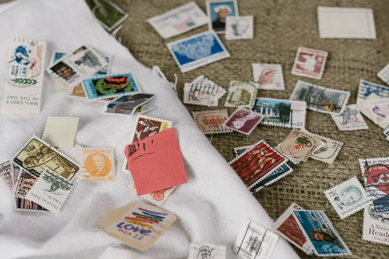 Assorted used postage stamps scattered across a white cloth and burlap surface