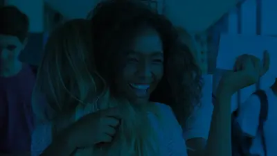 A student laughing as she hugs a friend in a school hallway