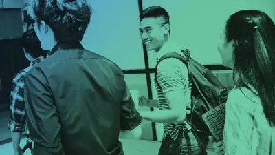 A student with a backpack smiling at classmates in a school hallway