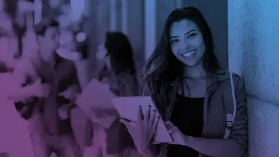 A smiling student holding a tablet in a busy school hallway