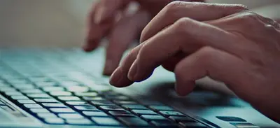 Close-up of a person's hands typing on a laptop keyboard