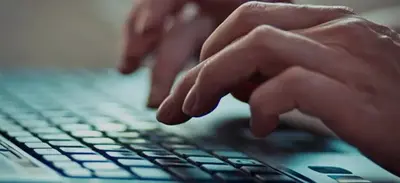 Close-up of a person's hands typing on a laptop keyboard