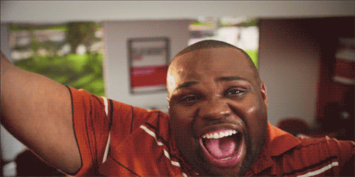 A man in a red shirt throws his arms wide and shouts with excitement.