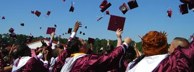 Graduates in maroon gowns tossing their caps into a clear blue sky