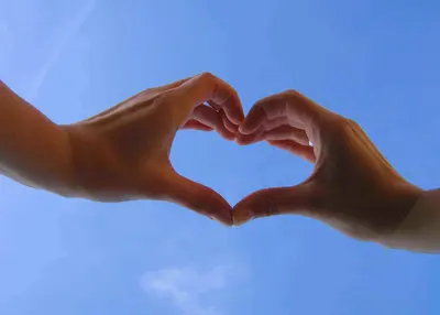 Two hands forming a heart shape against a clear blue sky