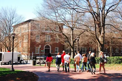 A group of students walking along a brick path toward a brick campus building on a sunny day.