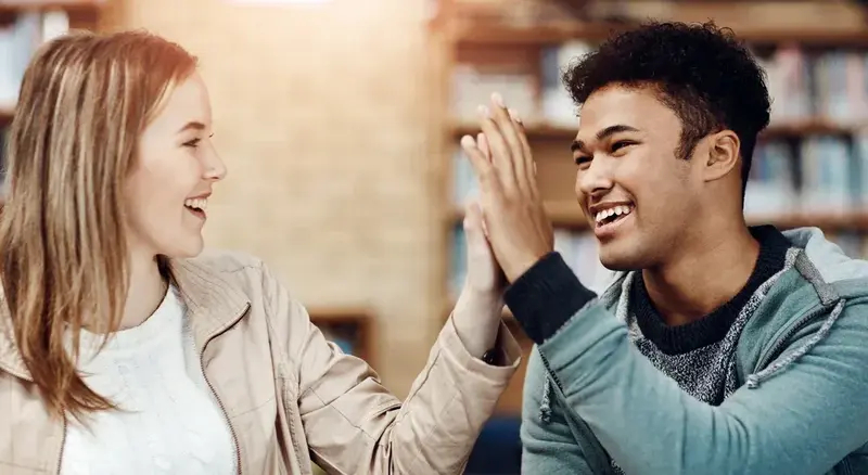 Two smiling high school students giving each other a high five in a library