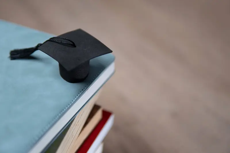 A miniature black graduation cap resting on the corner of a stack of books