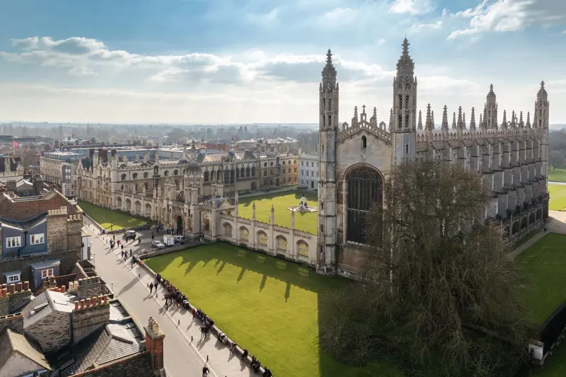 Aerial view of a Gothic university chapel with spires overlooking green lawns and historic college buildings