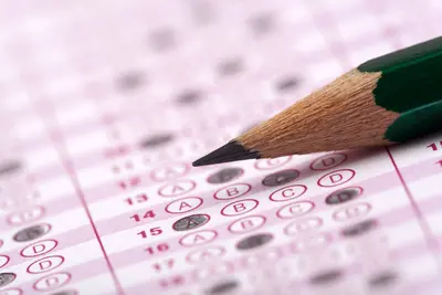 A sharpened pencil resting on a multiple-choice answer sheet with rows of A, B, C, D bubbles.