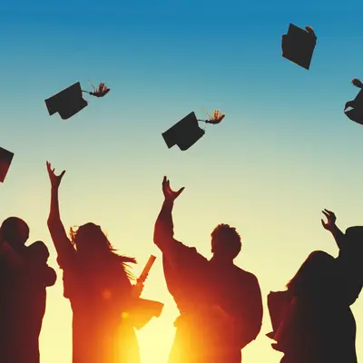 Silhouetted graduates tossing their caps into the air against a sunset sky