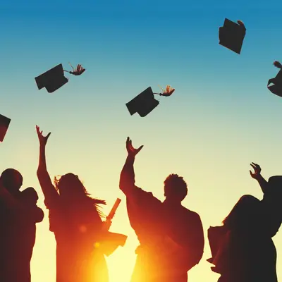 Silhouetted graduates tossing their caps into the air against a sunset sky