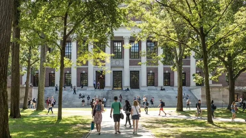 Students walking across a sunny tree-lined campus lawn toward a large columned brick library building.