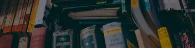 Dimly lit stacks of old books, including titles such as "The Newcomes," "Memoirs of a Field-Marshal" and "Tales After Supper"
